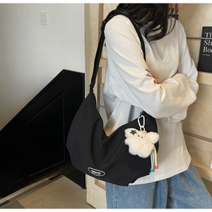 Dettaglio della borsa a mezzaluna in nylon nero con ciondolo a orsetto e patch logo