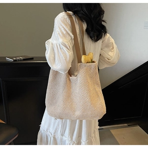 Detail of cream woven tote bag with brown leather straps held by model in white dress
