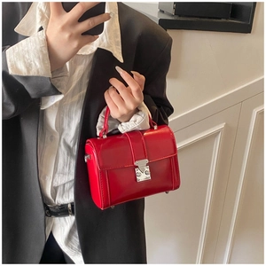 Close-up of bright red patent leather handbag with metal lock held by a model