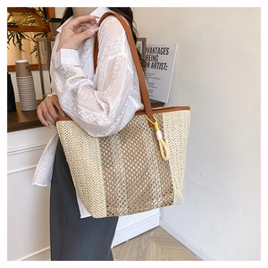 Detail of contrast woven straw beach tote bag featuring leather straps and yellow tassel