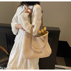 Close-up of beige woven tote bag with hollow mesh pattern and wide khaki shoulder strap