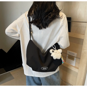 Dettaglio di una grande borsa hobo in tela nera con logo bianco e ciondolo a forma di orsetto