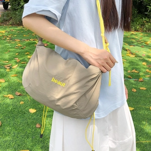 Outdoor model shot showing the khaki nylon crossbody bag with yellow drawstring strap