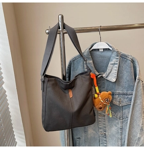 Détail du sac seau en toile grise avec bandoulière large, écusson et ours en peluche