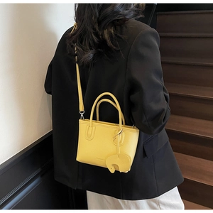 Close-up of yellow litchi grain leather handbag featuring a cute elephant charm