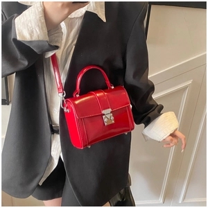 Detail of red glossy mini crossbody bag with silver buckle worn on a black suit