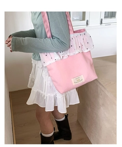 Detail of pink canvas tote bag with white floral lace trim and shoulder strap on model