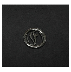 Close-up of metallic logo emblem on black textured fabric of the luxury backpack