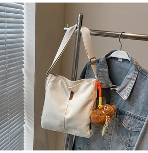 Détail du sac seau en toile blanche avec écusson en cuir et breloque ours marron