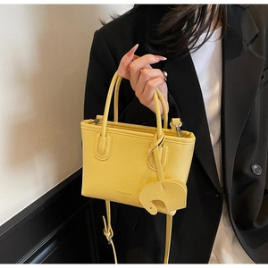 Detail of yellow litchi pattern mini tote with an elephant charm on a model's arm