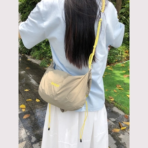 Outdoor shot of a khaki nylon drawstring crossbody bag with yellow beaut embroidery