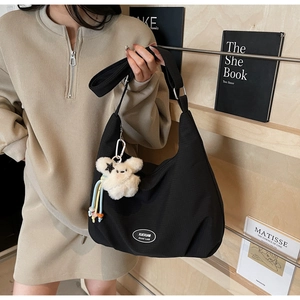 Black canvas underarm bag with a white plush puppy charm and an oval logo patch