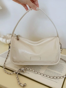 Elegant cream leather pillow bag with chain strap and handle shown in a minimalist setting