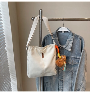 Détail d'un sac seau en toile blanche avec étiquette en cuir et pendentif ours