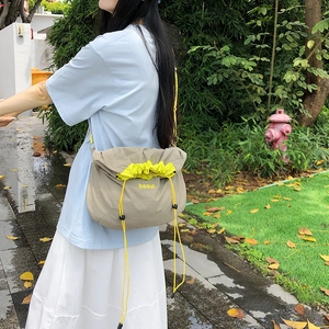 Detail of khaki nylon crossbody bag with neon yellow drawstring and beaut lettering print