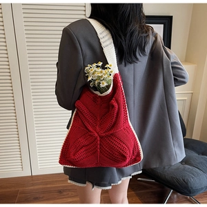 Detail of red crochet tote bag with white trim worn over a grey blazer indoors
