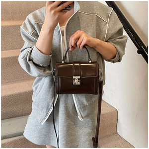 Detail of dark brown leather crossbody bag featuring silver metal lock and top handle