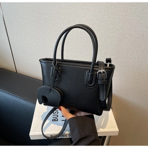 Detailed view of black litchi texture handbag with elephant charm and shoulder strap