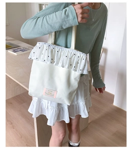 Detailed view of white canvas tote bag with floral ruffle trim on a model in a cozy office