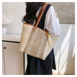Large beige woven straw tote bag with brown leather straps shown on a model