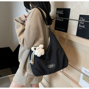 Detail of black nylon crossbody bag with cute plush pendant and oval brand logo detail