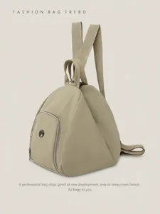 Detail view of khaki green triangular backpack featuring nylon fabric and circular metal logo