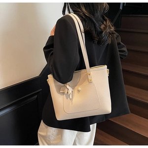 Close-up of off-white lychee leather tote bag featuring a decorative bow on the pocket