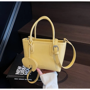 Close-up of yellow lychee grain leather tote bag with elephant charm and dual handles