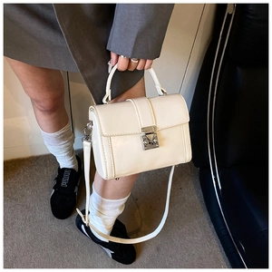Detail of cream crossbody bag with silver buckle held by model in urban style