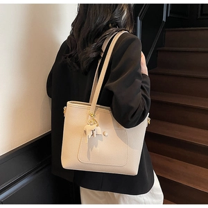 Detailed macro view of the cream leather texture and elephant charm on this tote bag