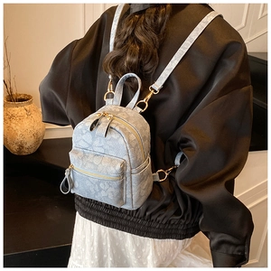 Detail of light blue denim mini backpack featuring floral patterns and gold hardware