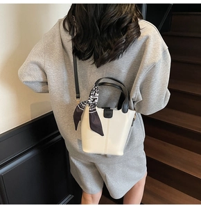 Rear view of model wearing a cream bucket bag with black leather handle and silk scarf