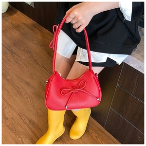 Macro detail of red pebbled leather shoulder bag featuring a decorative bow accent