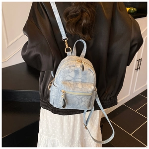 Detail of light blue floral denim mini backpack featuring gold zippers and metal hardware