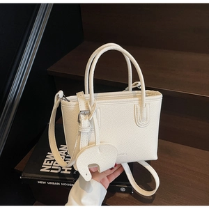 Close-up of white lychee pattern leather bucket bag with cute elephant charm on wooden stairs