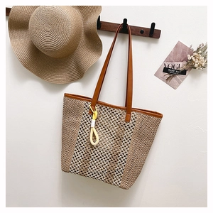Detail of a large straw tote bag in beige and brown weave with a yellow ring charm
