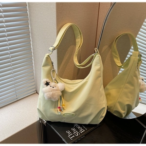 Close-up of light green textured canvas crescent bag with cute plush bear charm accessory
