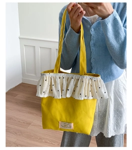 Detail of yellow canvas tote bag with white floral ruffle trim and fabric label