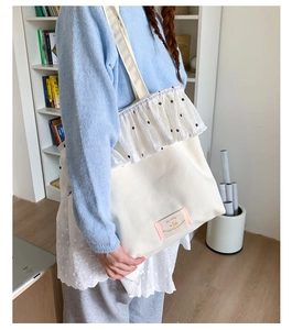 Detail of white canvas shoulder bag featuring polka dot ruffle trim and textile label
