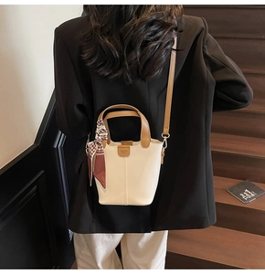 Chic cream bucket bag with silk scarf detail worn by model on wooden stairs