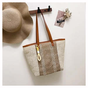 Detail of woven straw beach tote bag hanging on wooden hook with leather straps