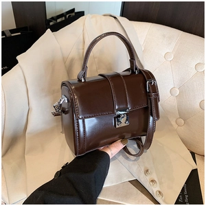 Detailed view of dark brown patent leather satchel bag with silver clasp and top handle