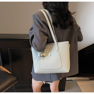 Close-up of light grey litchi leather tote bag with bow charm on a model's shoulder