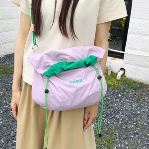 Outdoor model shot of a purple nylon drawstring crossbody bag with green beaut embroidery