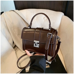 Detail of dark brown leather crossbody bag with silver buckle on a soft seat