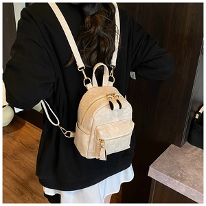 Detailed view of beige mini backpack with embossed floral pattern and gold hardware