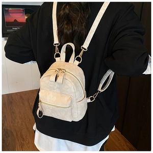 Detail of a mini cream-white PU leather backpack with subtle patterns and gold metal zippers