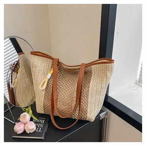 Detail of woven straw beach tote featuring brown leather handles and decorative ball