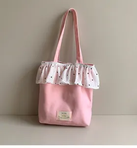 Detail of pink canvas tote bag featuring white floral ruffle trim and decorative patch