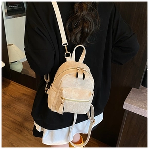 Rear view of model wearing a textured beige mini backpack with floral embossing